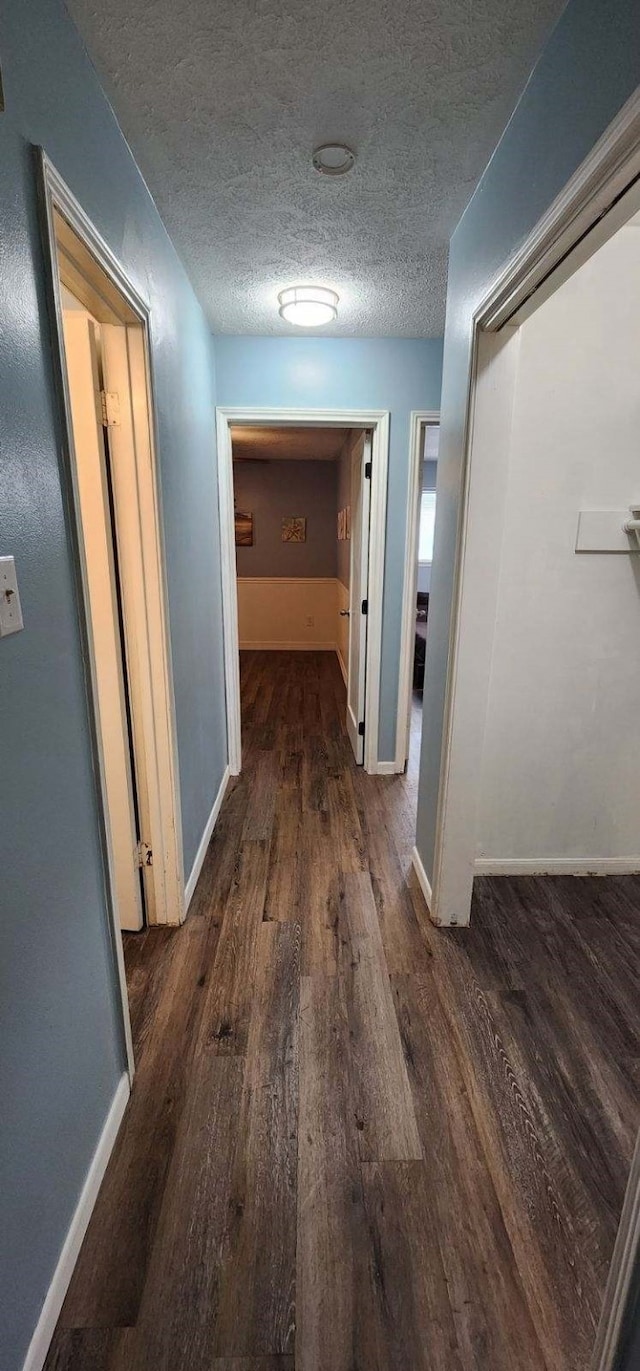 hall featuring wood finished floors, a textured ceiling, and baseboards