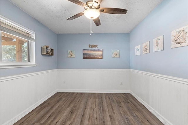 spare room featuring wood finished floors, a textured ceiling, a wainscoted wall, and a ceiling fan