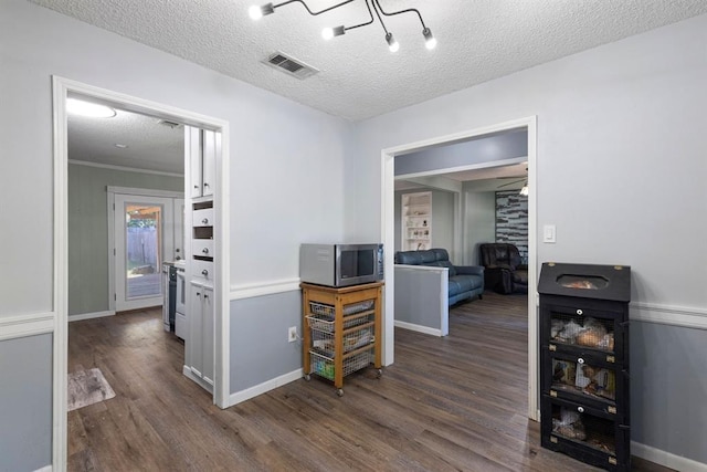 hall with baseboards, wood finished floors, visible vents, and a textured ceiling