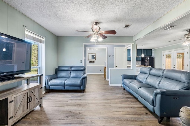 living room with baseboards, a ceiling fan, visible vents, and light wood-style flooring