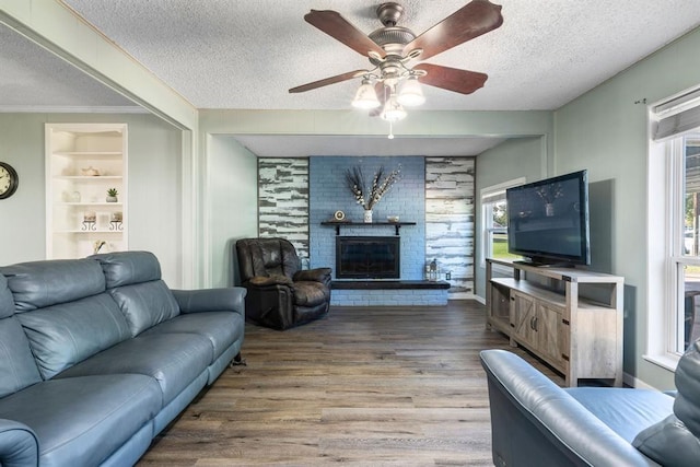 living room featuring ceiling fan, a brick fireplace, wood finished floors, and a textured ceiling