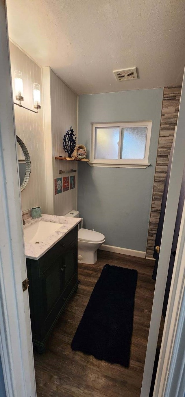 half bath featuring a textured ceiling, toilet, visible vents, wood finished floors, and vanity