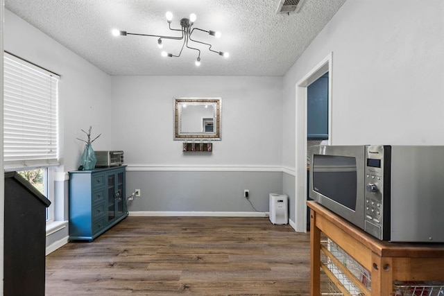 kitchen featuring wood finished floors, visible vents, stainless steel microwave, a textured ceiling, and a notable chandelier