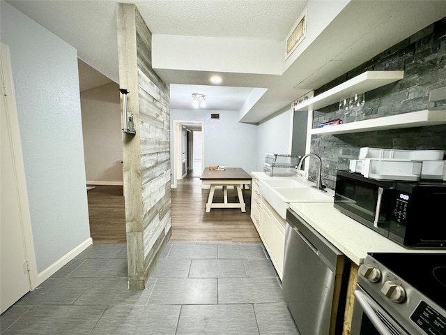 kitchen featuring a sink, baseboards, white cabinetry, light countertops, and appliances with stainless steel finishes