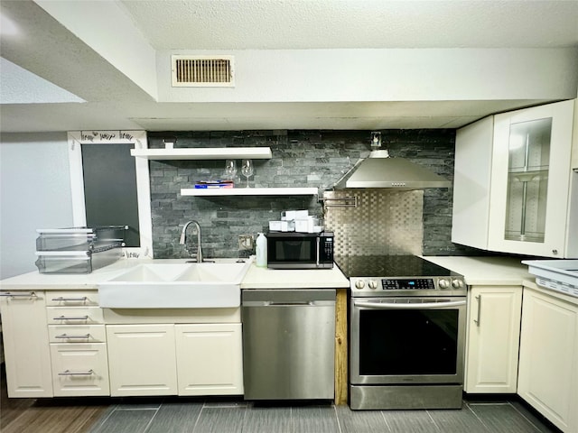 kitchen with white cabinets, wall chimney range hood, visible vents, a sink, and appliances with stainless steel finishes