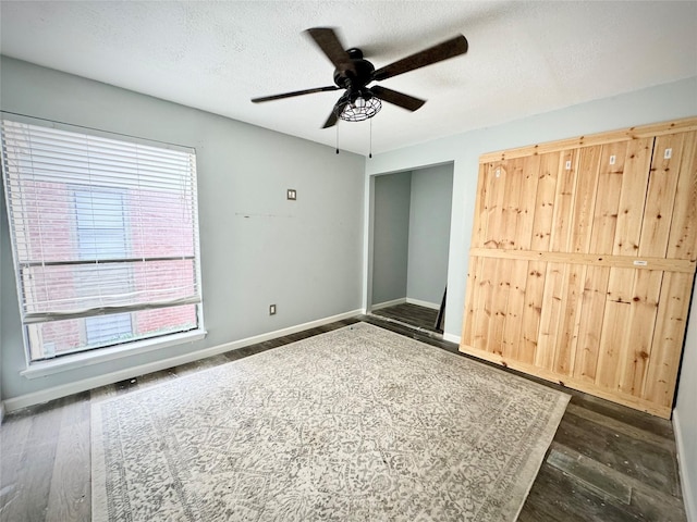 unfurnished bedroom featuring baseboards, a textured ceiling, ceiling fan, and dark wood-style flooring
