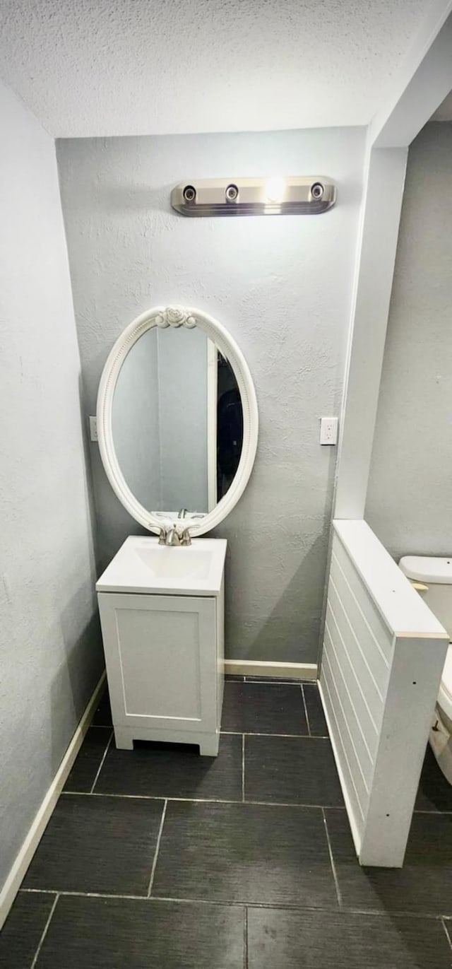 half bathroom featuring tile patterned floors, a textured ceiling, toilet, baseboards, and vanity