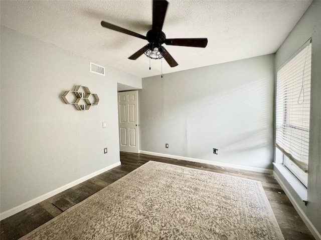 unfurnished room featuring dark wood-style floors, a textured ceiling, visible vents, and plenty of natural light