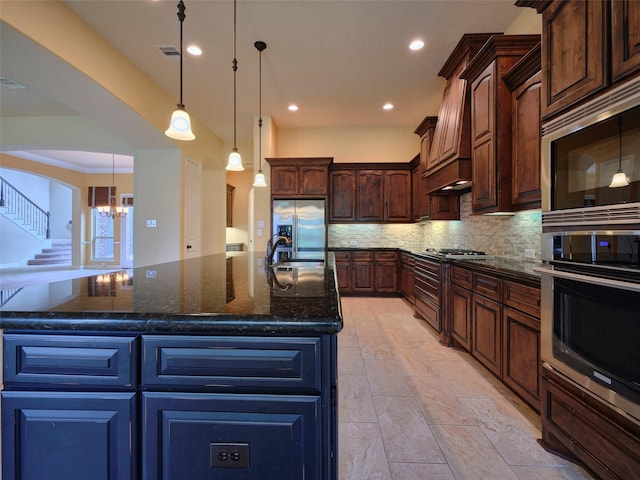 21315 Whistle Wood Dr, Richmond, TX 77406 - kitchen with backsplash, dark stone counters, a kitchen island with sink, appliances with stainless steel finishes, and a notable chandelier