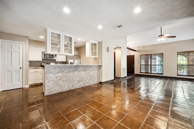 interior space with a textured ceiling, ceiling fan, visible vents, and baseboards