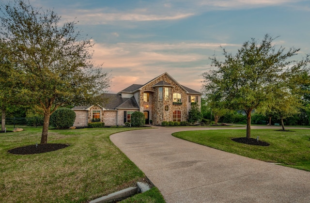 view of front of property with a lawn, brick siding, stone siding, and curved driveway