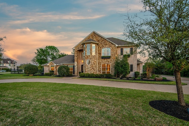 french country style house featuring a lawn, stone siding, and curved driveway