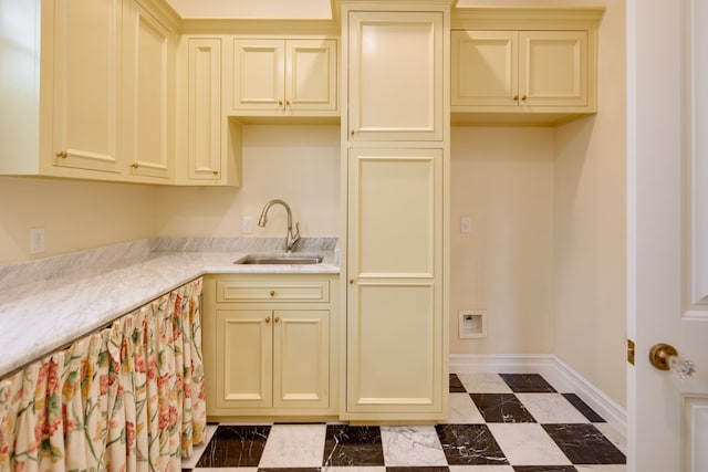 kitchen featuring light countertops, baseboards, cream cabinets, and a sink