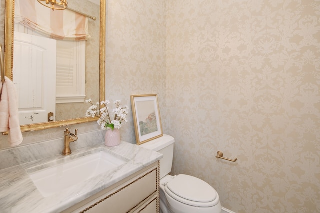 half bathroom featuring toilet, vanity, and wallpapered walls