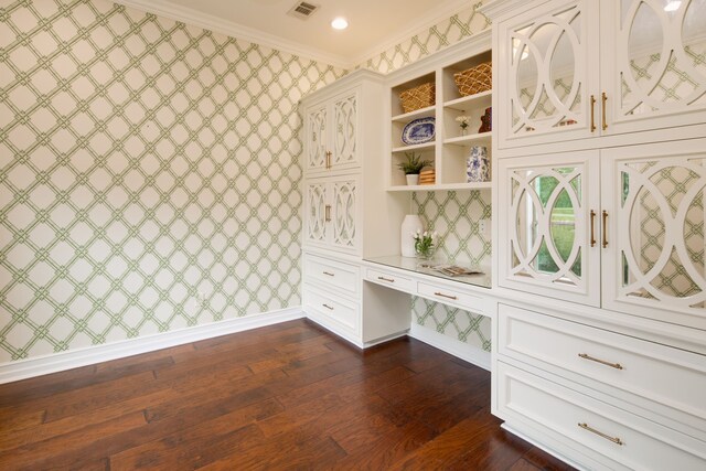 mudroom featuring built in desk, wallpapered walls, visible vents, ornamental molding, and dark wood-style flooring