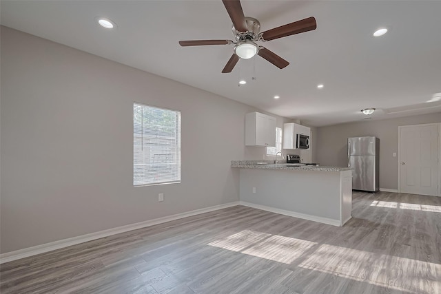 kitchen with a peninsula, light wood-type flooring, white cabinetry, and stainless steel appliances