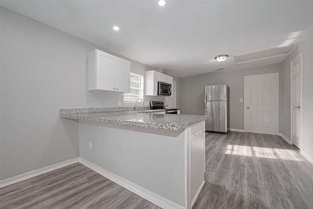 kitchen with wood finished floors, white cabinetry, baseboards, a peninsula, and appliances with stainless steel finishes