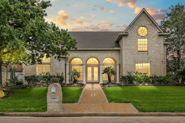 french country home featuring a lawn, brick siding, a shingled roof, and french doors