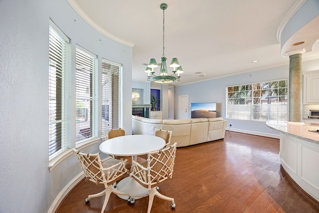 dining room featuring baseboards, a notable chandelier, a lit fireplace, wood finished floors, and ornamental molding