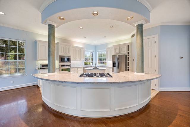 kitchen with dark wood finished floors, stainless steel appliances, a spacious island, decorative columns, and tasteful backsplash