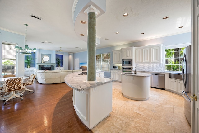 kitchen featuring stainless steel appliances, a kitchen island with sink, open floor plan, ornate columns, and ornamental molding