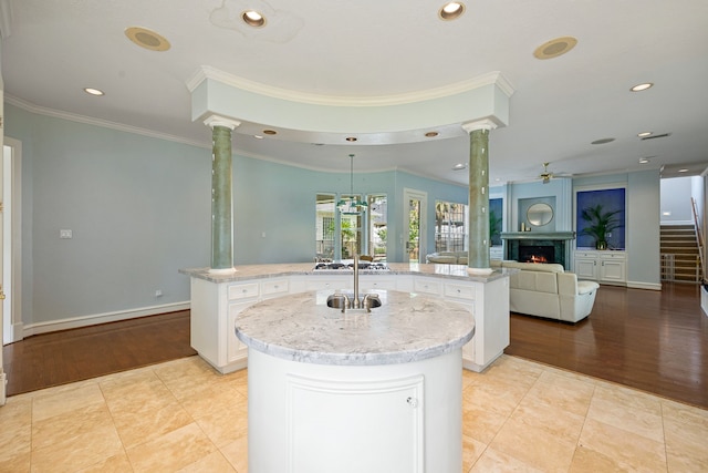 kitchen featuring a warm lit fireplace, a ceiling fan, a kitchen island with sink, and ornate columns