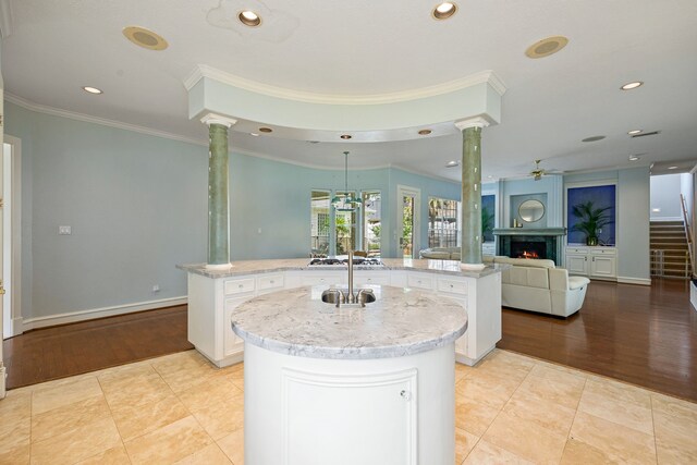 13602 Copeland Oaks Blvd, Cypress, TX 77429 - kitchen featuring a center island with sink, ornate columns, a lit fireplace, ceiling fan, and white cabinetry