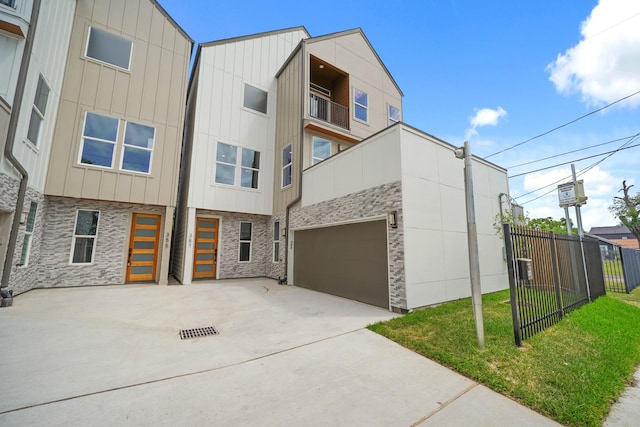 view of front of house featuring stone siding, fence, board and batten siding, and concrete driveway