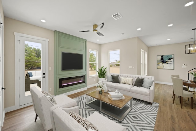 living room with a healthy amount of sunlight, ceiling fan with notable chandelier, visible vents, and light wood-type flooring