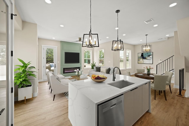 kitchen with a healthy amount of sunlight, stainless steel dishwasher, a sink, light wood-style floors, and a chandelier