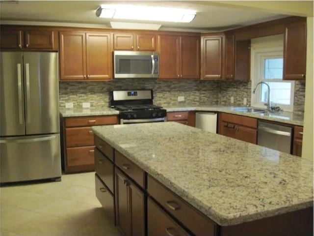 kitchen featuring light stone counters, a sink, decorative backsplash, appliances with stainless steel finishes, and a kitchen island