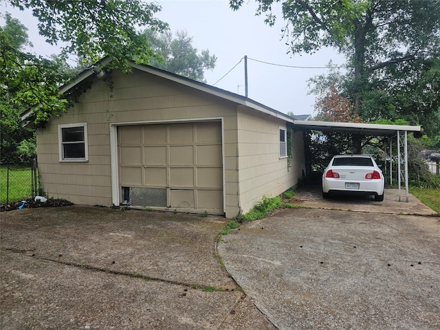 detached garage featuring driveway, fence, and an attached carport