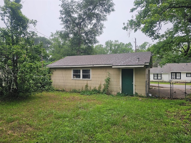 rear view of property with fence, a lawn, and roof with shingles
