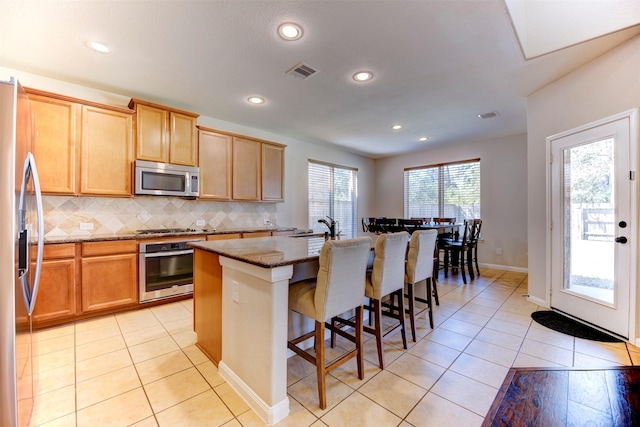 5002 Sawmill Terrace Ln, Spring, TX 77389 - kitchen with appliances with stainless steel finishes, dark stone counters, backsplash, an island with sink, and light tile patterned flooring