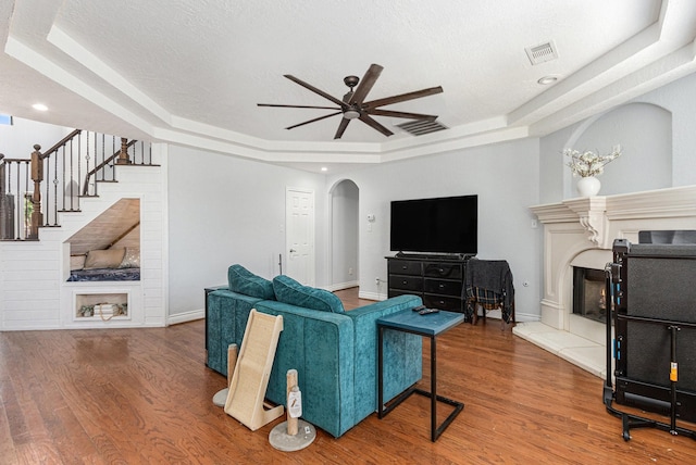 living room featuring wood finished floors, ceiling fan, arched walkways, a tray ceiling, and visible vents