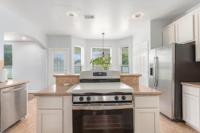 kitchen with arched walkways, light tile patterned flooring, stainless steel appliances, and visible vents