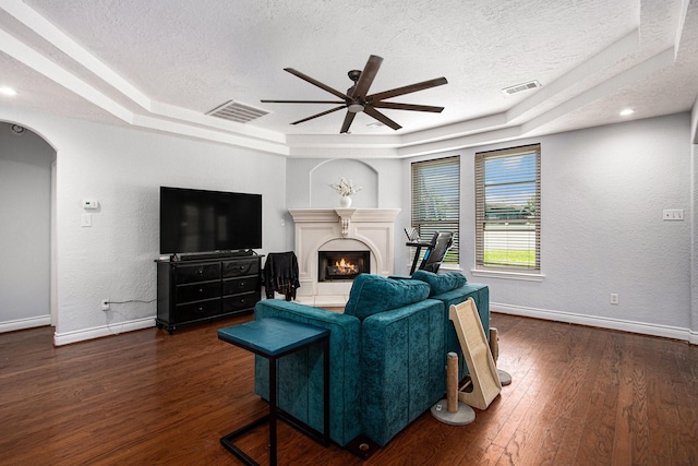 living room with a tray ceiling, a textured ceiling, ceiling fan, and visible vents
