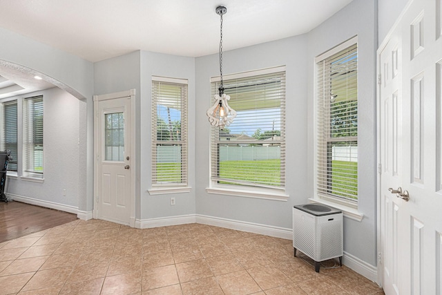 unfurnished dining area featuring arched walkways, baseboards, and light tile patterned flooring