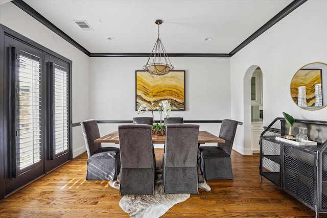 dining area featuring wood finished floors, visible vents, arched walkways, and crown molding