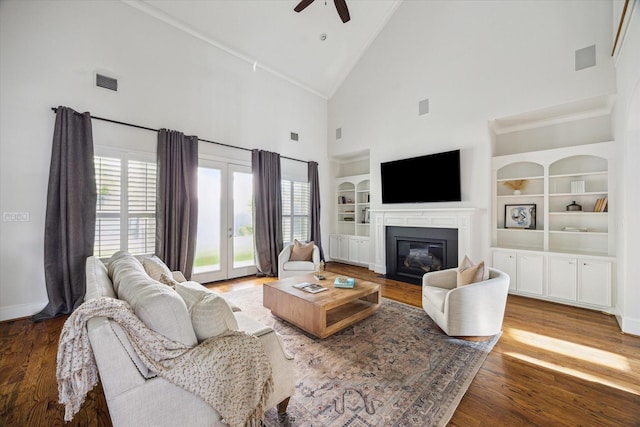 living area featuring visible vents, built in shelves, wood finished floors, ceiling fan, and high vaulted ceiling