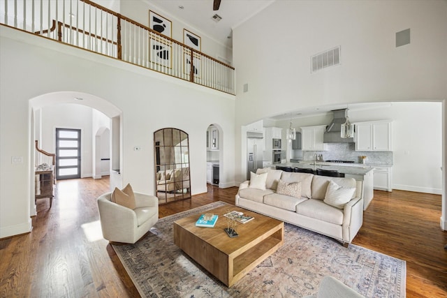 living area with arched walkways, wood finished floors, visible vents, and a high ceiling