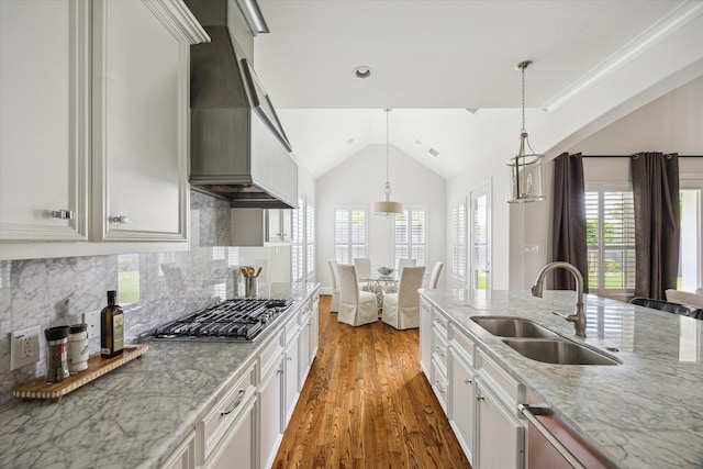 kitchen with a sink, light wood-type flooring, vaulted ceiling, custom exhaust hood, and appliances with stainless steel finishes