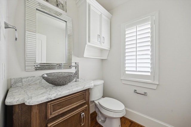 half bath with toilet, vanity, wood finished floors, and baseboards