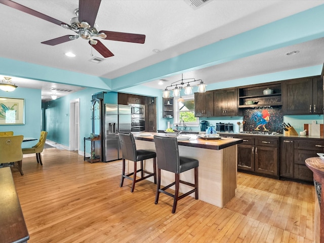 kitchen with dark brown cabinets, stainless steel appliances, open shelves, and light wood finished floors