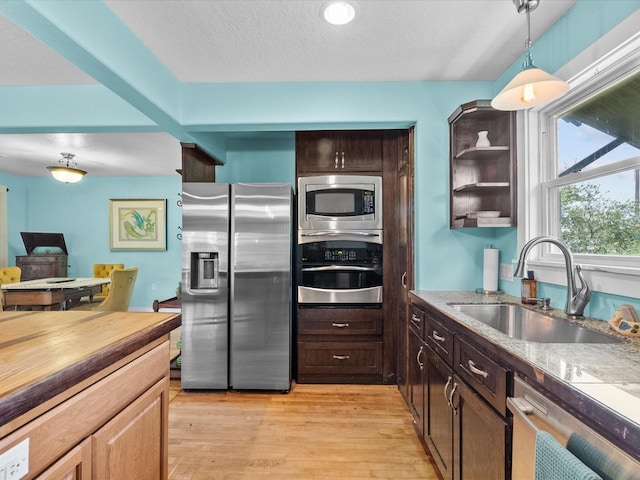 kitchen featuring hanging light fixtures, stainless steel appliances, a sink, light wood-type flooring, and a textured ceiling