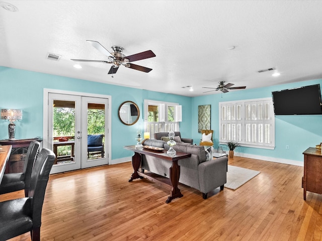 living area featuring light wood-style flooring, plenty of natural light, ceiling fan, visible vents, and french doors