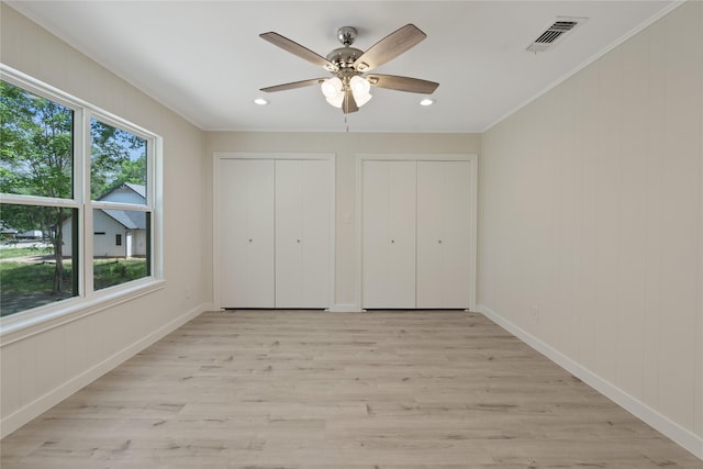 unfurnished bedroom with ornamental molding, multiple closets, multiple windows, and light wood-style flooring