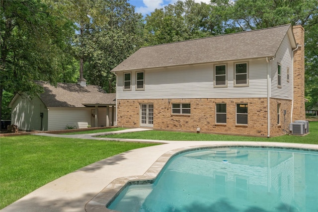 rear view of house with a lawn, brick siding, central AC unit, and an outdoor pool