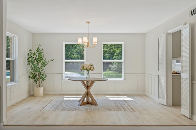 dining space with visible vents, wood finished floors, a wainscoted wall, a notable chandelier, and a decorative wall