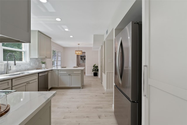 kitchen with appliances with stainless steel finishes, a sink, light wood finished floors, gray cabinets, and a peninsula
